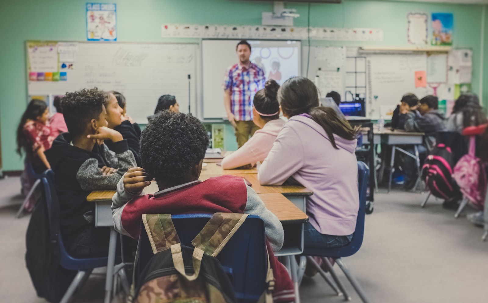 A middle-school classroom: students at their desks, a teacher at the whiteboard